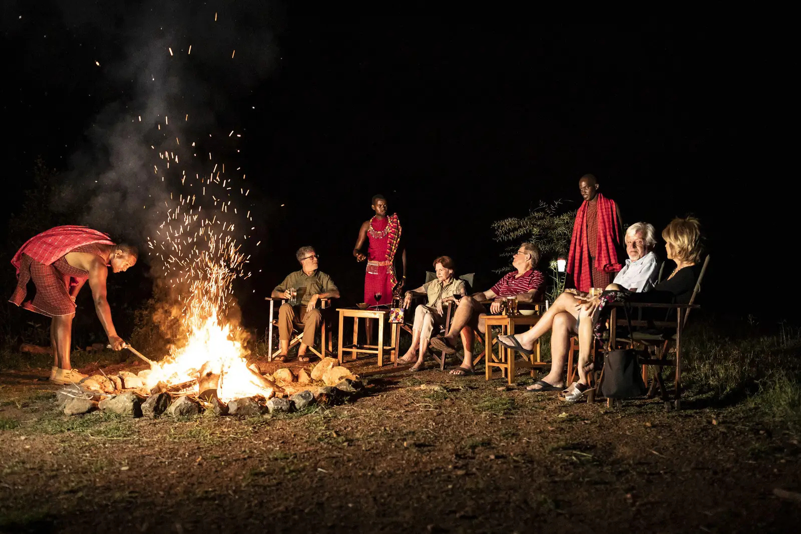 Guests around a campfire at night with Maasai hosts.