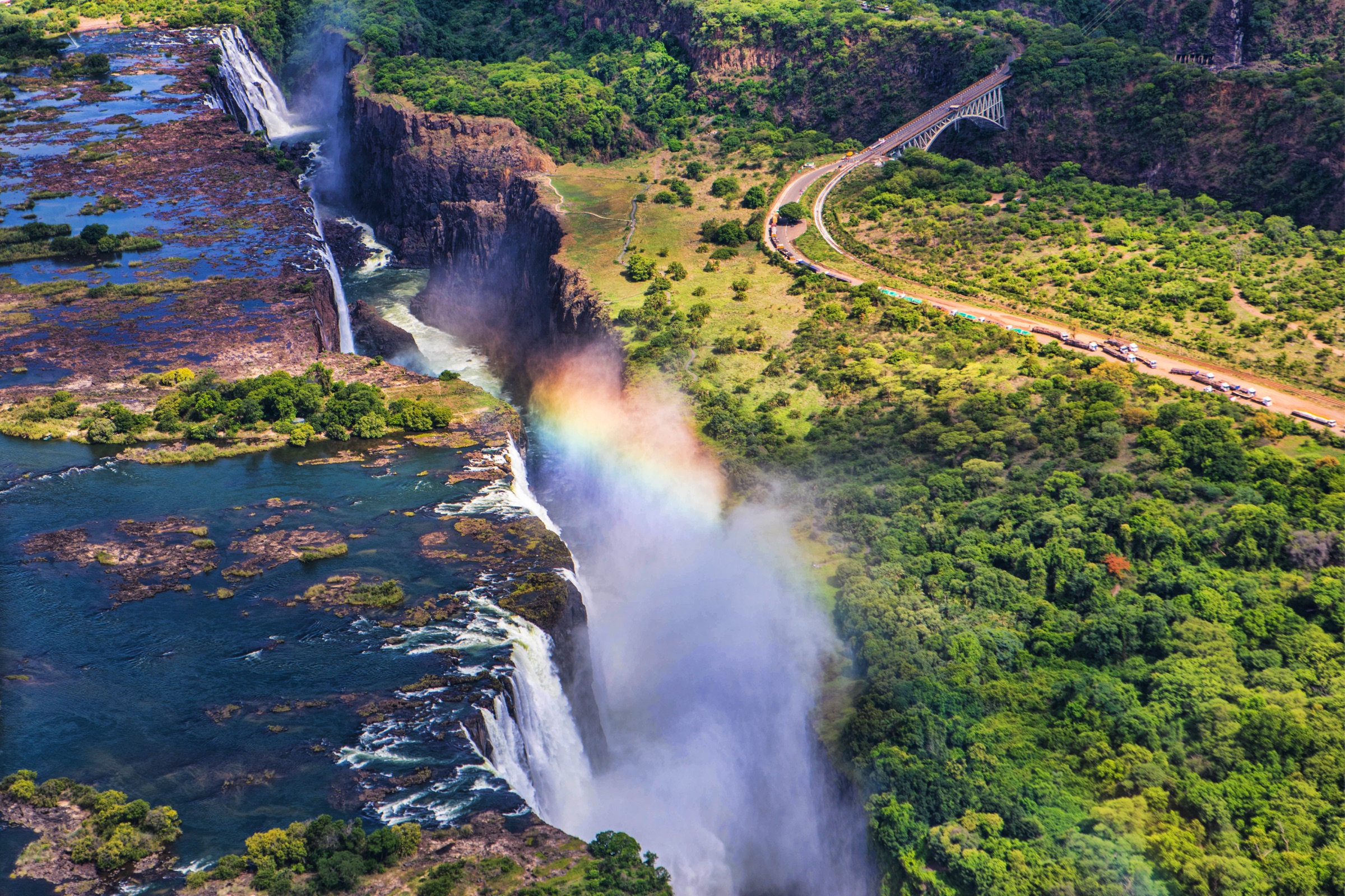 Aerial view of Victoria Falls in full flow, rainbow over the gorge.