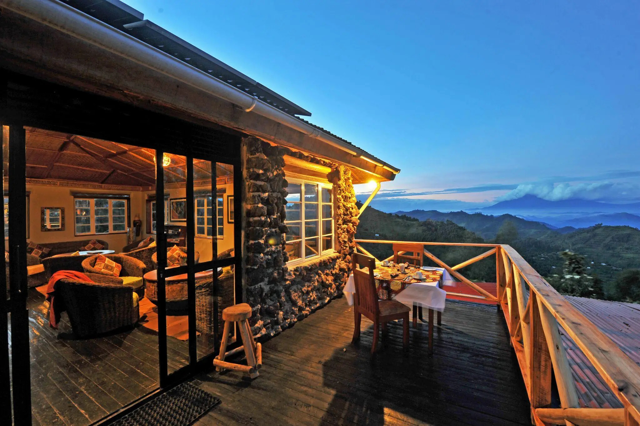 A lodge deck at golden hour, Virunga volcanoes silhouetted in the distance.
